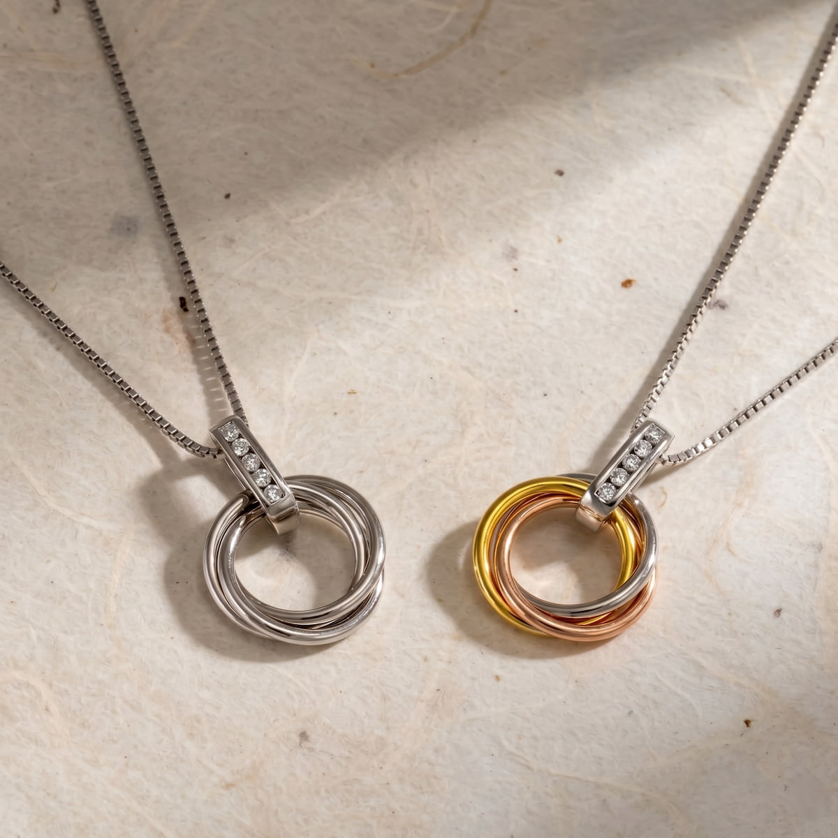 Pair of entwined circle pendants on delicate sterling silver chains, one in silver and the other in mixed gold vermeil tones, each accented with sparkling lab grown diamonds.