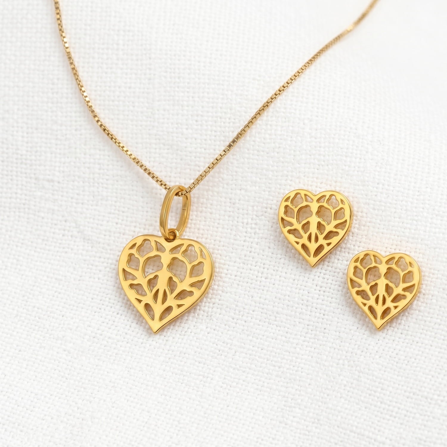 Gold vermeil heart-shaped stud earrings with detailed filigree inspired by Yorkshire, paired with a matching pendant on a fine chain, displayed on soft linen fabric.