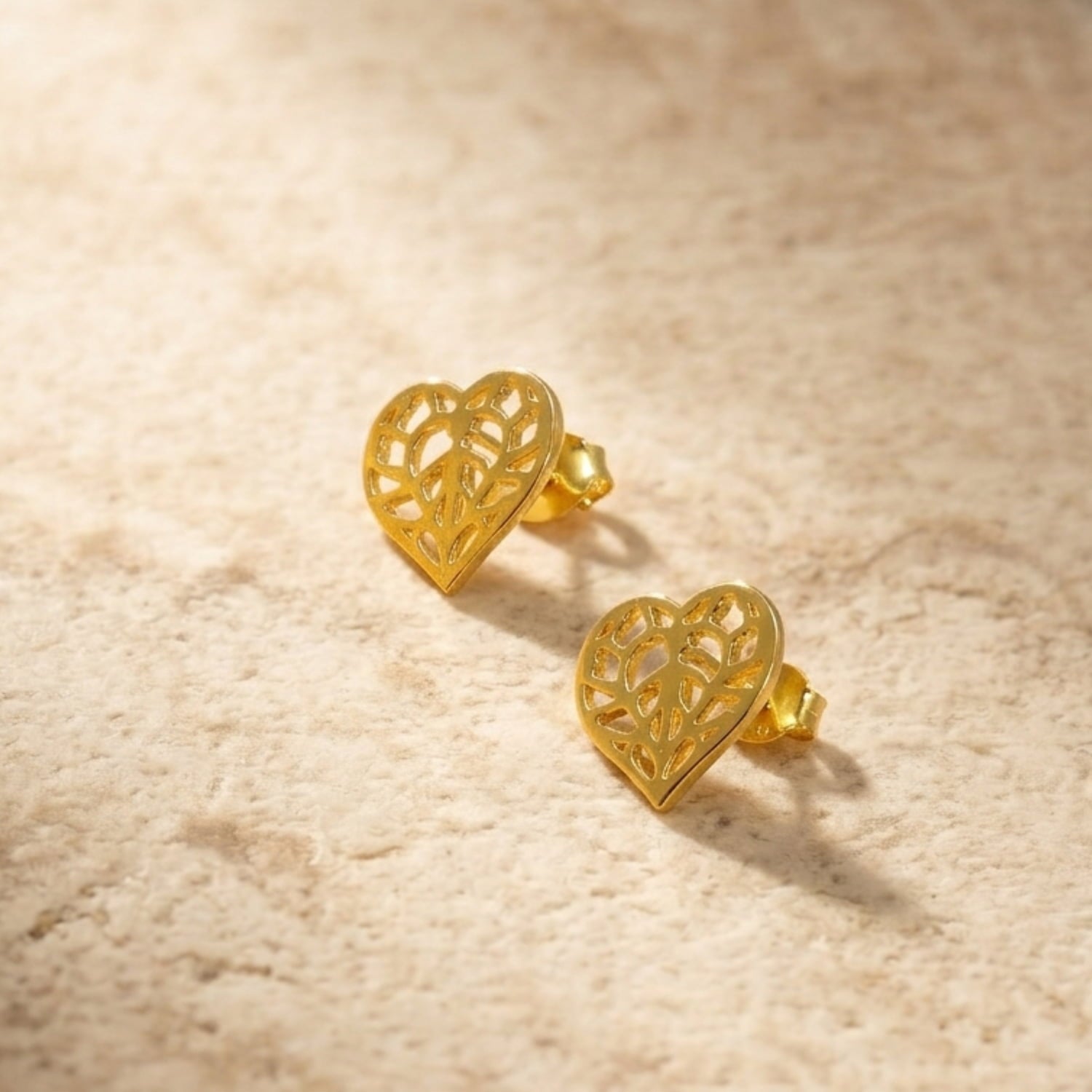 Pair of gold vermeil heart-shaped stud earrings featuring intricate Yorkshire-inspired filigree detailing, displayed on a natural stone surface, embodying elegant British craftsmanship.