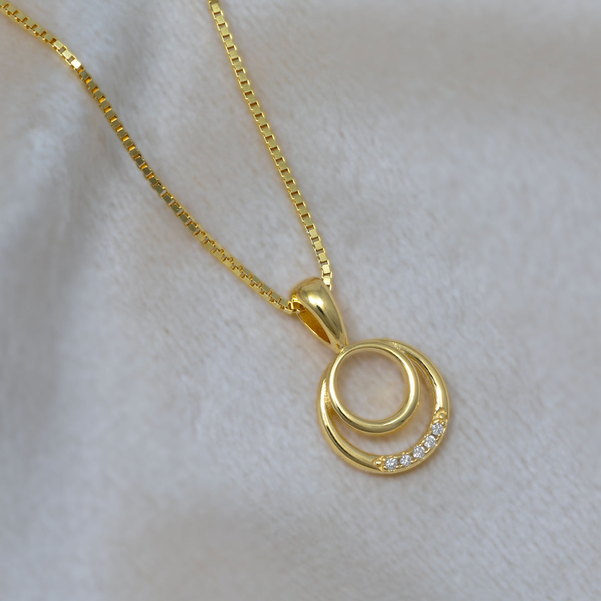 Gold vermeil pendant necklace featuring two interlocking circles, one adorned with small lab grown diamonds, suspended from a fine gold chain on a neutral cream fabric.
