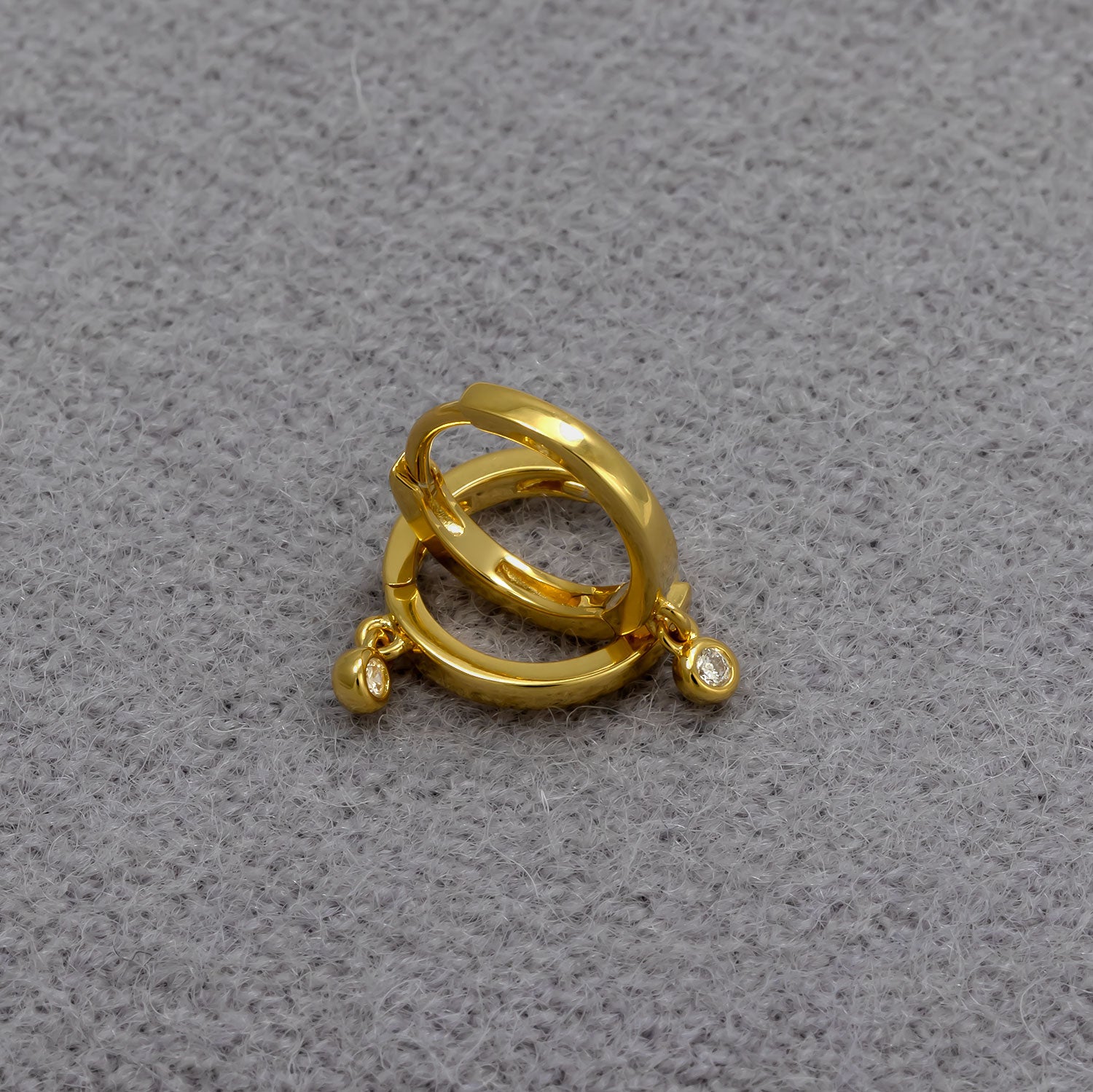 Pair of gold vermeil hinged hoop earrings featuring small round lab grown diamond charms, displayed on a soft grey textured fabric surface.