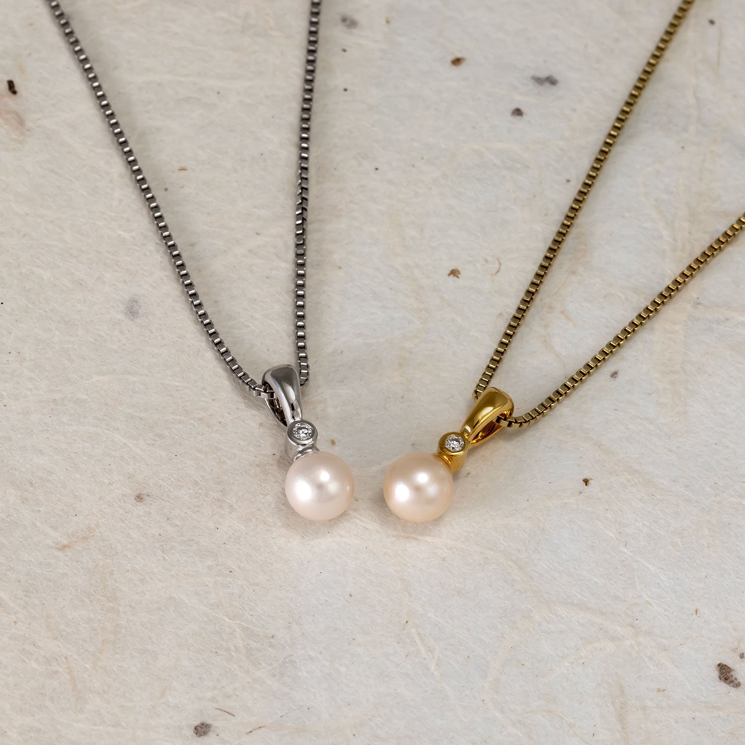 Pair of elegant sterling silver and gold vermeil pendants each featuring a freshwater pearl and a small lab grown diamond set above, displayed on a neutral textured surface.