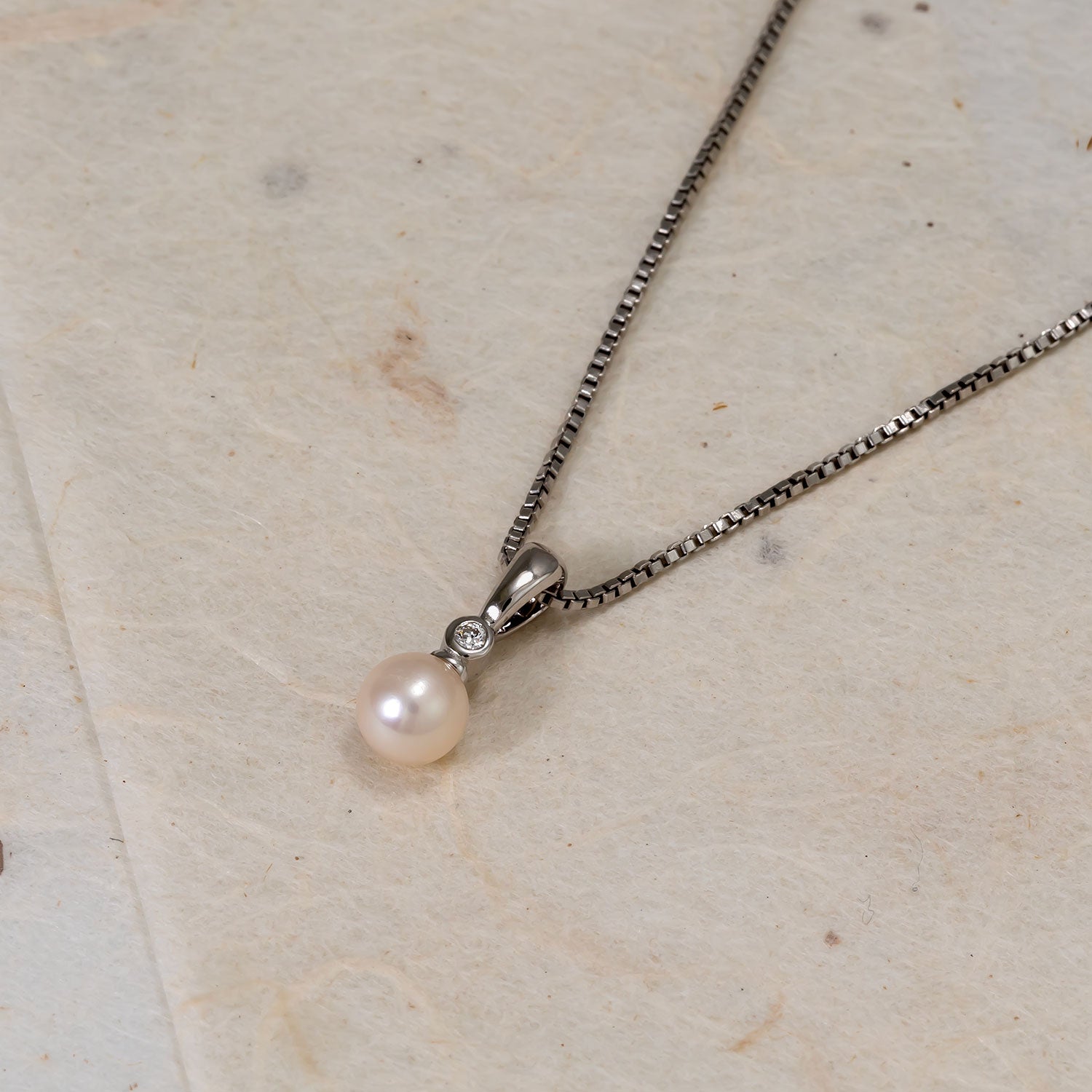 Sterling silver pendant necklace featuring a luminous freshwater pearl accented by a small lab grown diamond, suspended from a fine box chain on a neutral textured surface.