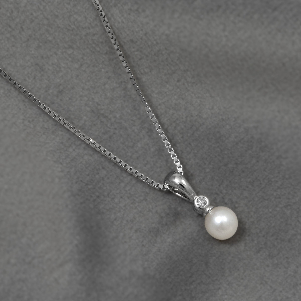 Sterling silver pendant necklace featuring a lustrous freshwater pearl accented with a small lab grown diamond, displayed on a soft grey fabric background.