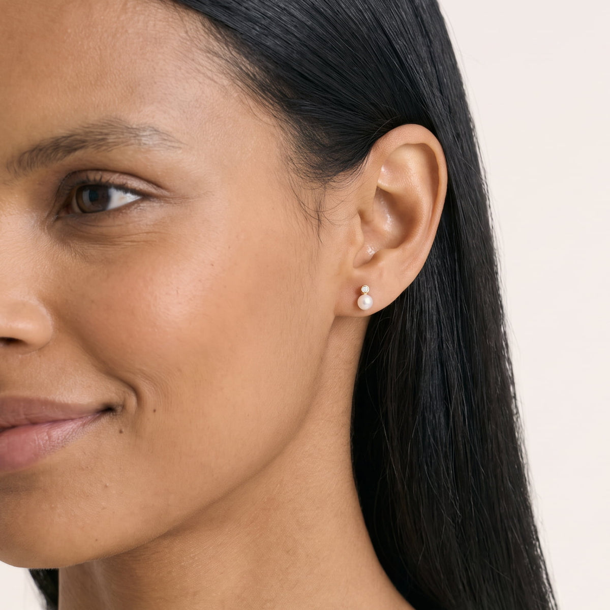 Model wears a pair of gold vermeil stud earrings featuring lustrous freshwater pearls beneath small lab-grown diamond accents, combining classic elegance with contemporary fine jewelery design.