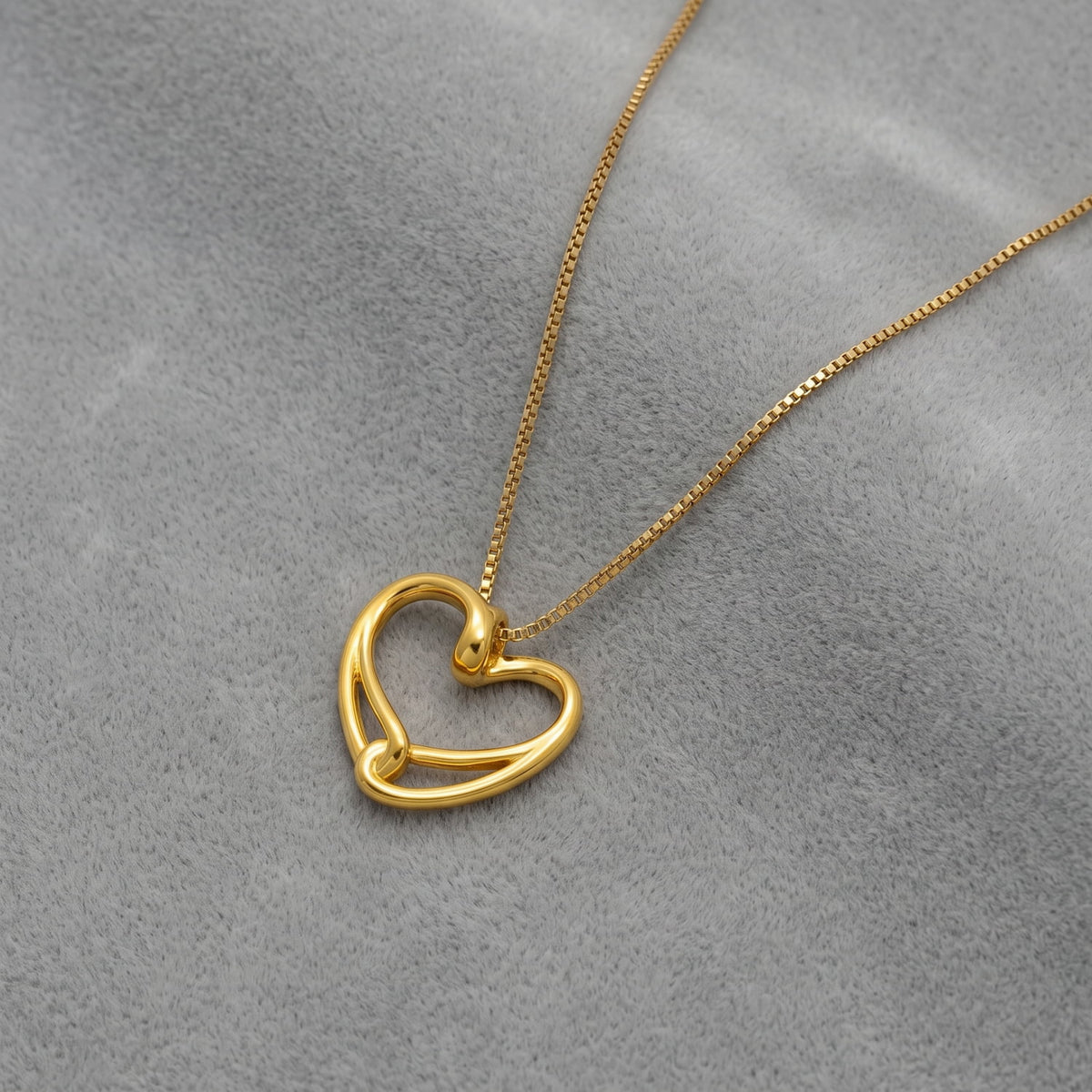 A gold vermeil heart-shaped pendant necklace, displayed on a textured gray velvet surface.