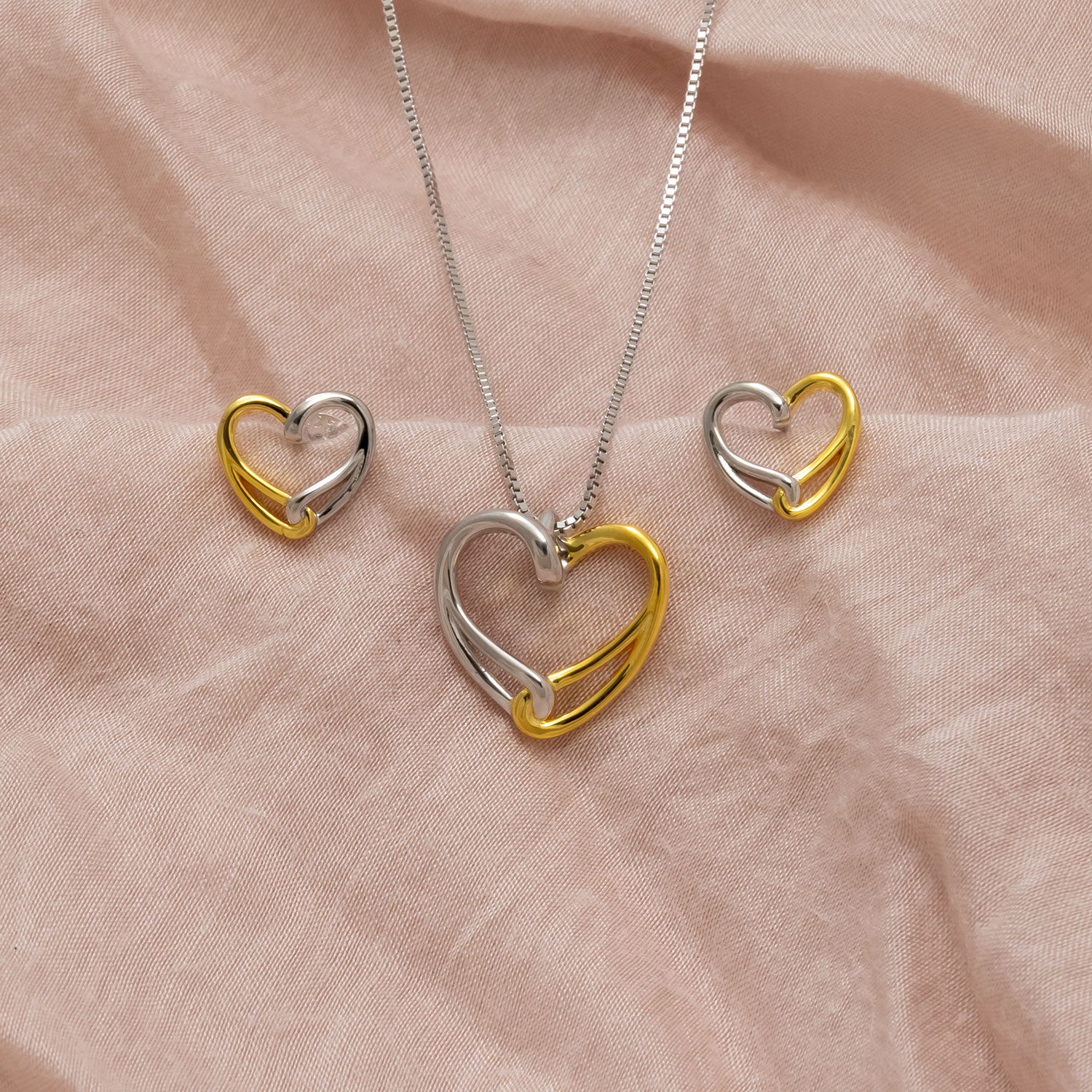Contemporary sterling silver and gold vermeil earrings paired with a matching pendant, each featuring an intertwined heart design with smooth polished finishes.