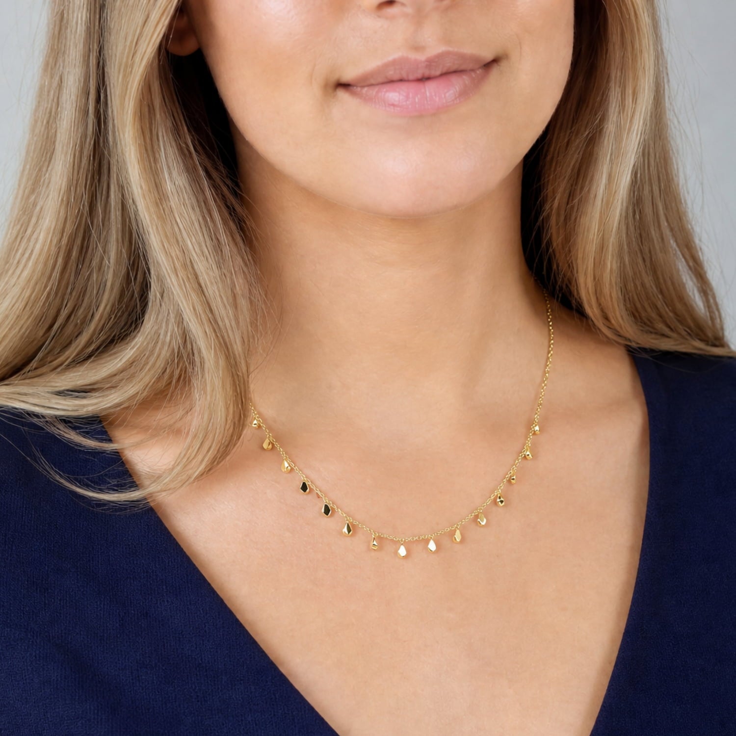 Model wears delicate gold vermeil necklace featuring multiple small dangling raindrop-shaped charms along a fine adjustable chain, showcasing subtle sculptural elegance.
