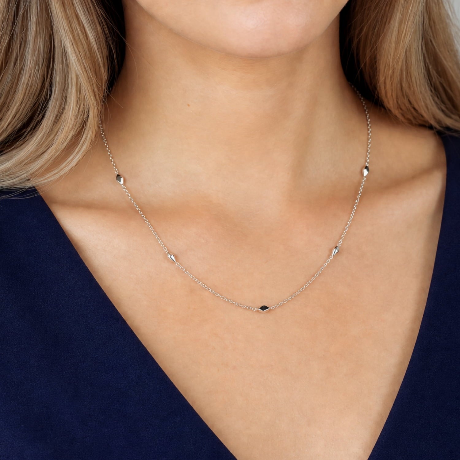 Model wears delicate sterling silver necklace featuring a series of smooth, scattered raindrop-shaped beads along a fine chain.