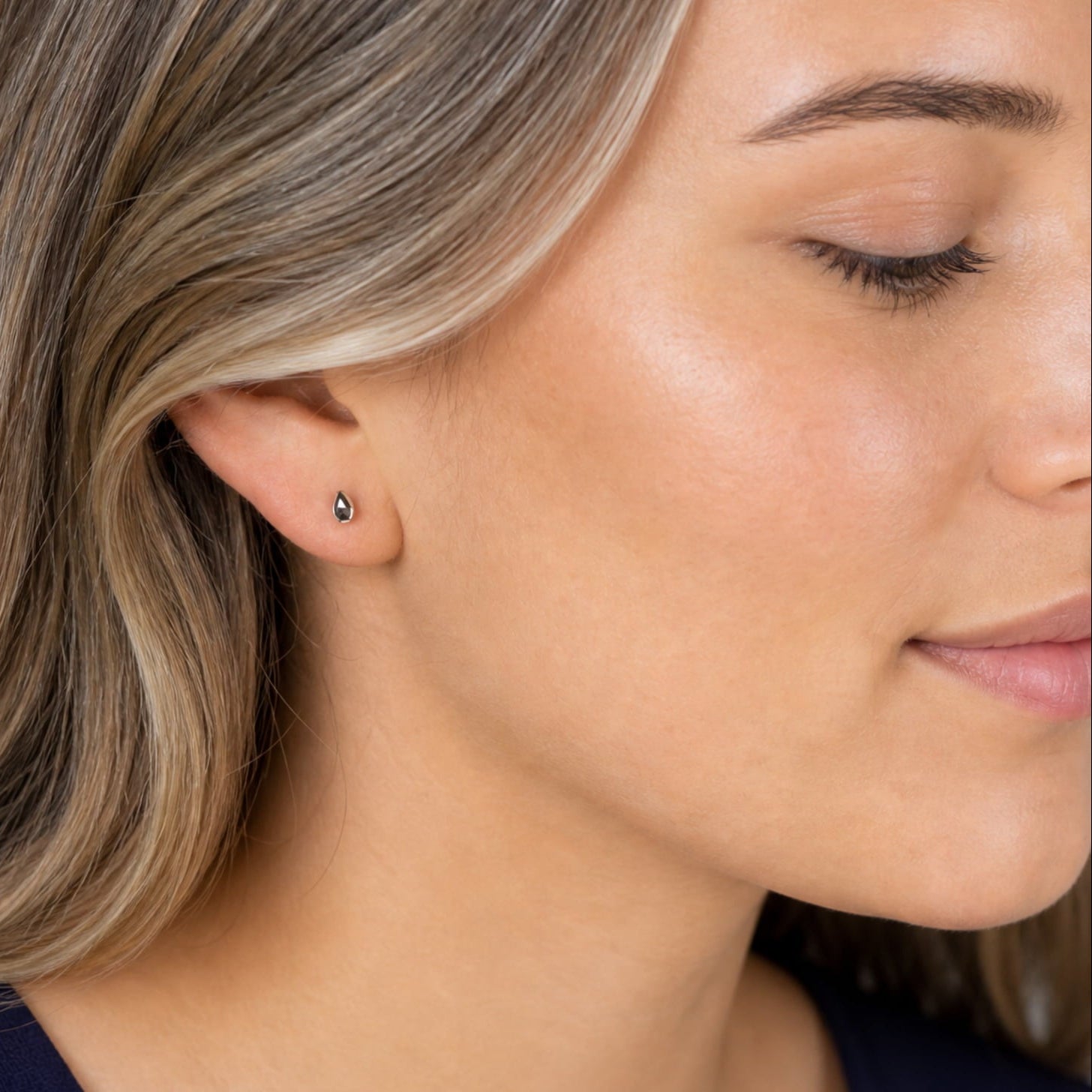Close-up of a woman wearing a small sterlign silver teardrop stud earring.
