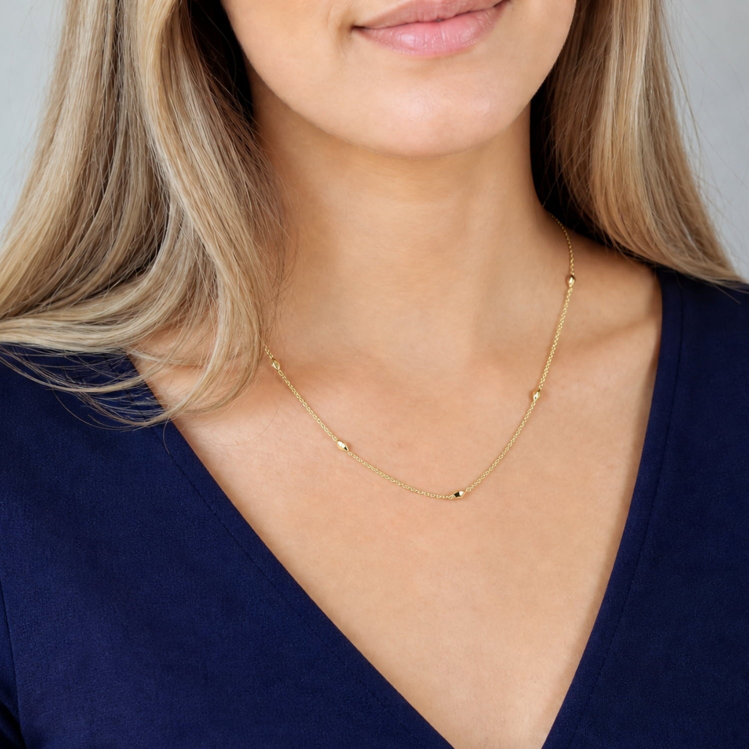 Model wears delicate gold vermeil necklace featuring scattered polished raindrop-shaped beads along a fine chain with an adjustable extension, combining simplicity with sculptural elegance.