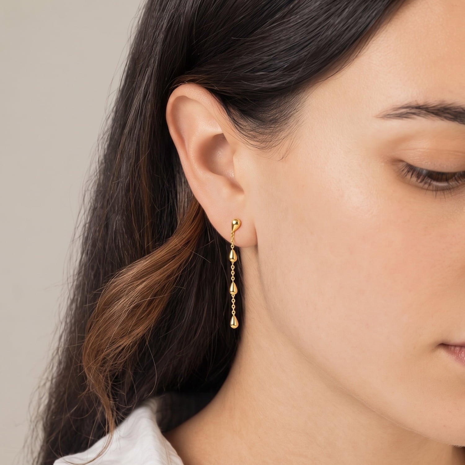 Close-up of a woman wearing gold vermeil dangling teardrop earrings with a neutral background