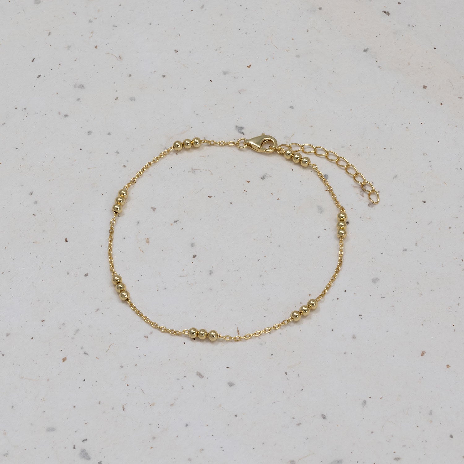 Delicate gold vermeil bracelet featuring a fine chain accented with three small bead clusters and an adjustable extension clasp, displayed on a neutral stone surface.
