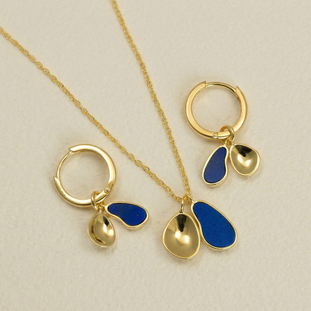 Gold vermeil hoop earrings and matching necklace featuring sculptural double pendants with deep blue lapis accents, displayed on a neutral textured background.