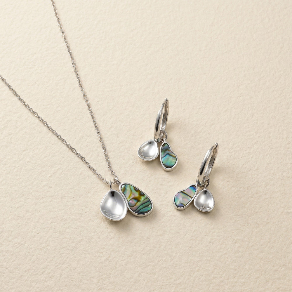 Sterling silver necklace and hoop earrings featuring paired teardrop-shaped charms, one with iridescent abalone shell and the other polished silver, showcasing contemporary elegance.