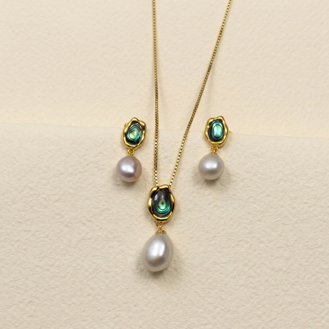 Gold vermeil drop earrings featuring vibrant abalone shells paired with single white pearls, displayed alongside a matching pendant necklace for a cohesive silver jewellery set.