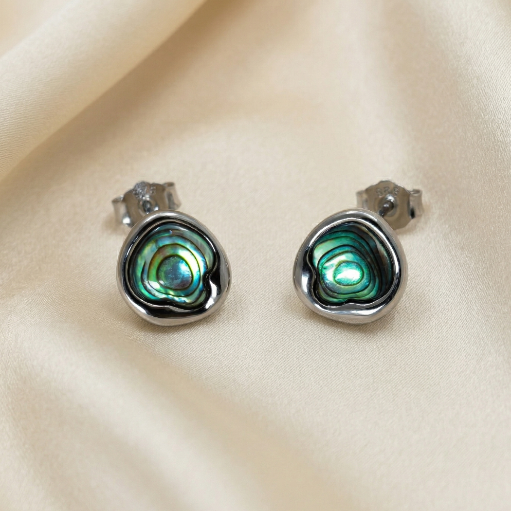 Pair of sterling silver stud earrings featuring vibrant abalone shells with organic, swirling patterns, displayed on a soft cream fabric background.