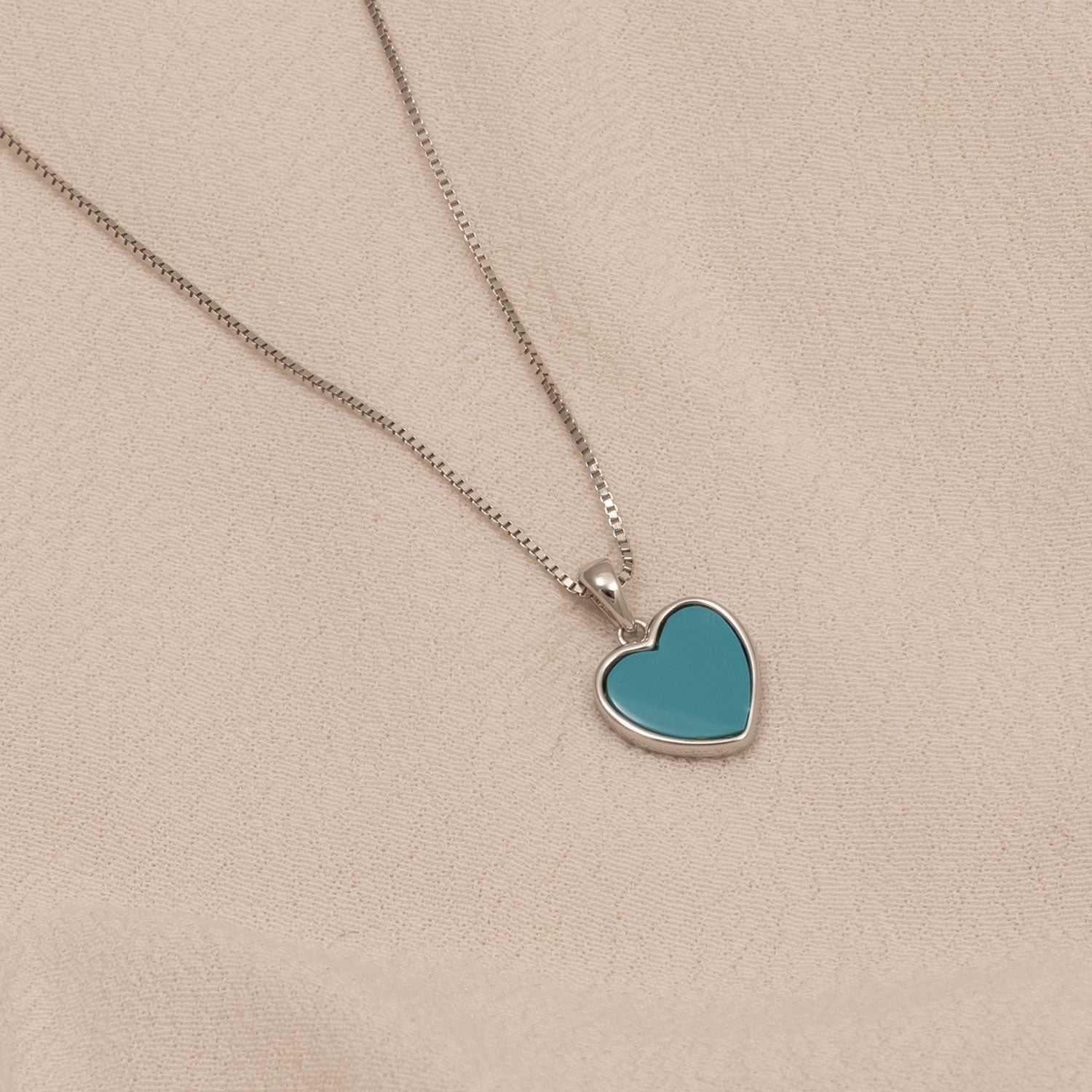Sterling silver necklace featuring a smooth turquoise heart-shaped pendant displayed on a soft neutral fabric background, highlighting contemporary British design.
