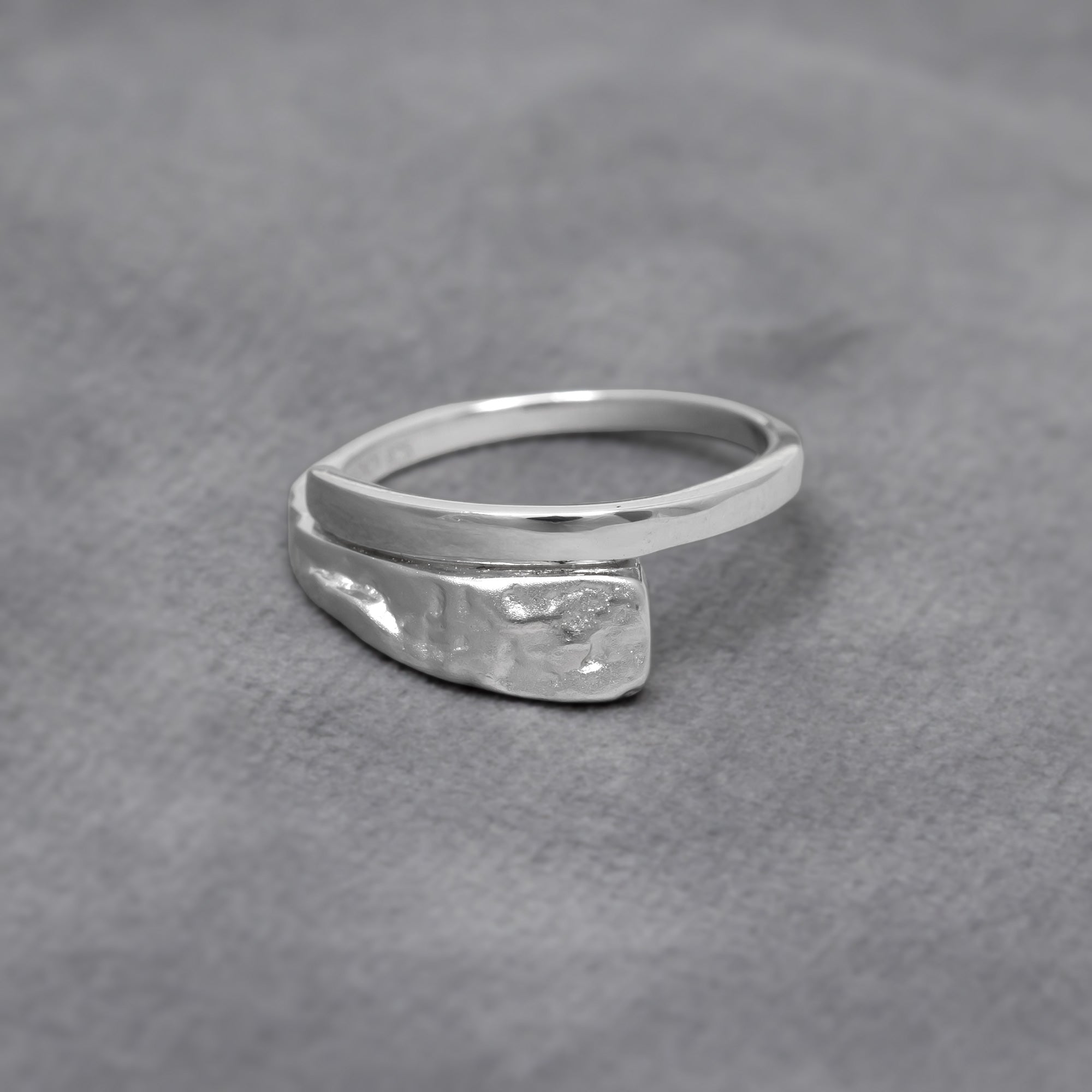 Sterling silver ring featuring a combination of polished and textured finishes with a sculptural form, reflecting contemporary British silver jewellery design. Placed on a grey velvet cloth.