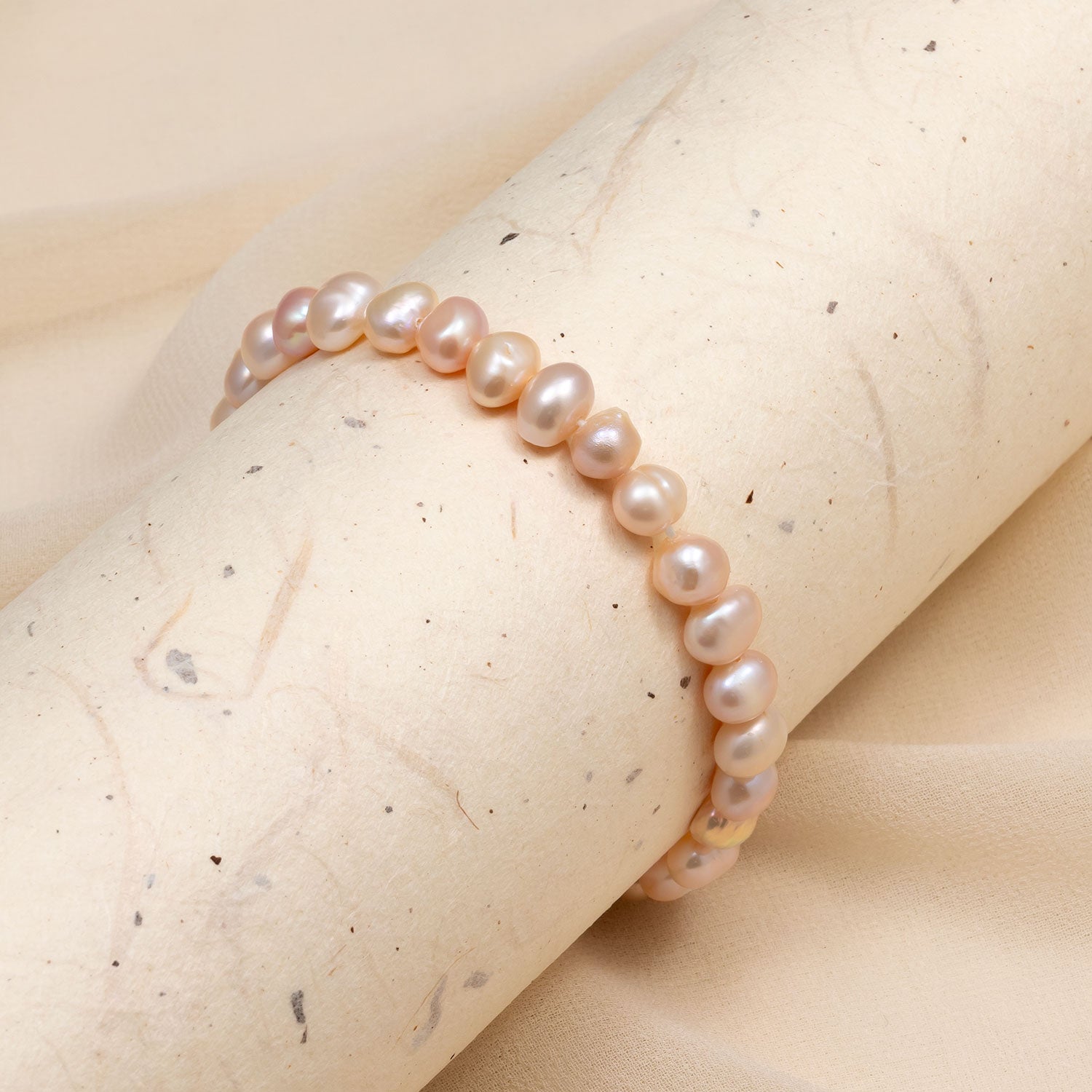 Delicate stretch bracelet featuring lustrous pink freshwater pearls with a soft sheen, presented on a neutral stone surface highlighting its elegant simplicity.