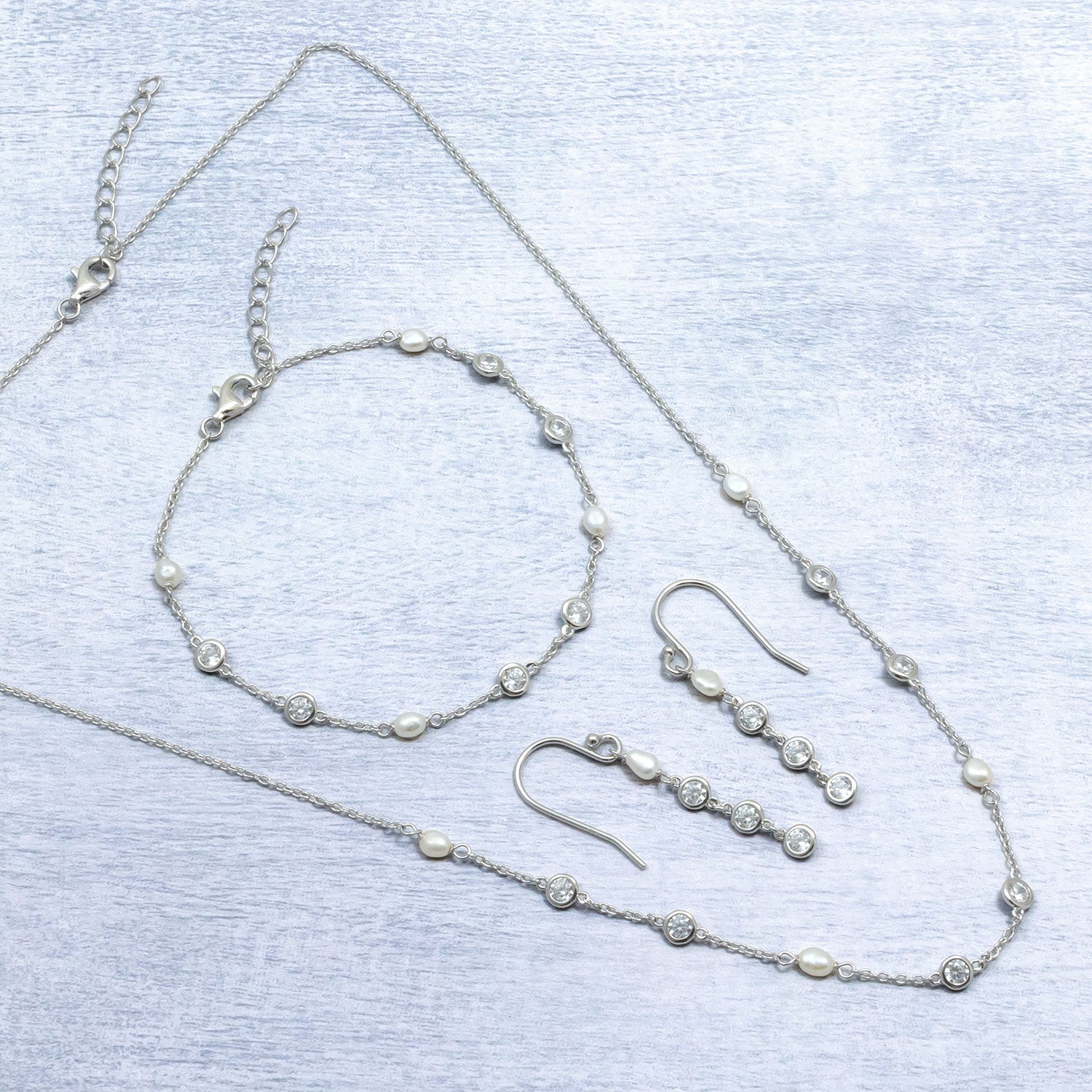 Set of sterling silver jewellery featuring drop earrings, a bracelet, and a necklace with alternating freshwater pearls and clear cubic zirconia stones for an elegant, sculptural look.