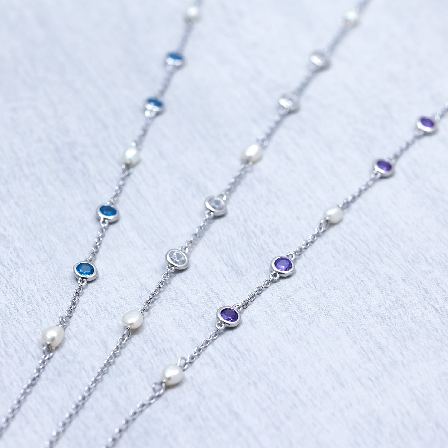 Three sterling silver chain necklaces featuring alternating freshwater pearls and bezel-set cubic zirconia stones in blue, clear, and purple hues, showcasing elegant minimalist design.