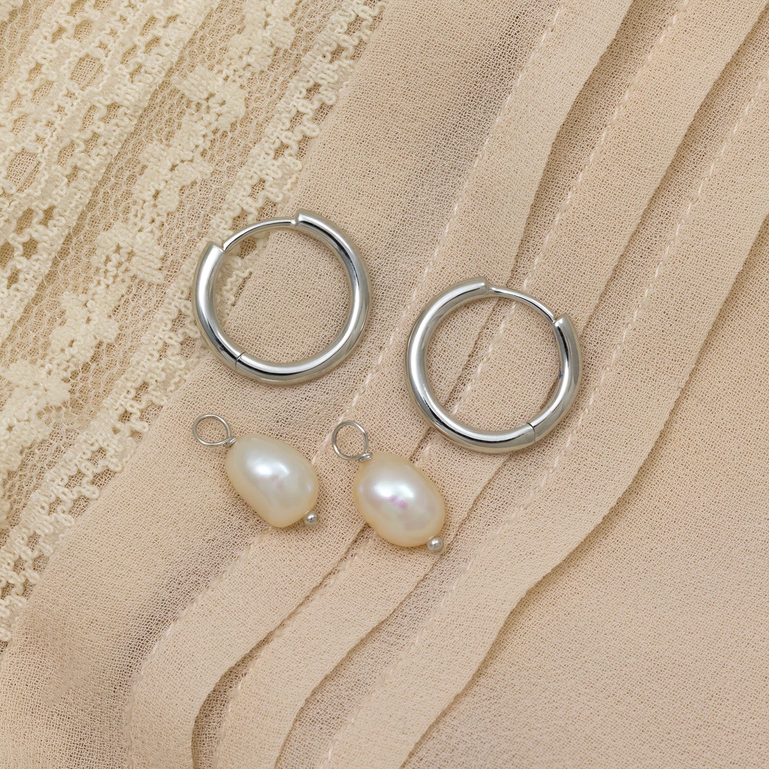Pair of polished sterling silver hinged hoops paired with smooth freshwater pearl charms, displayed on a textured beige fabric background.