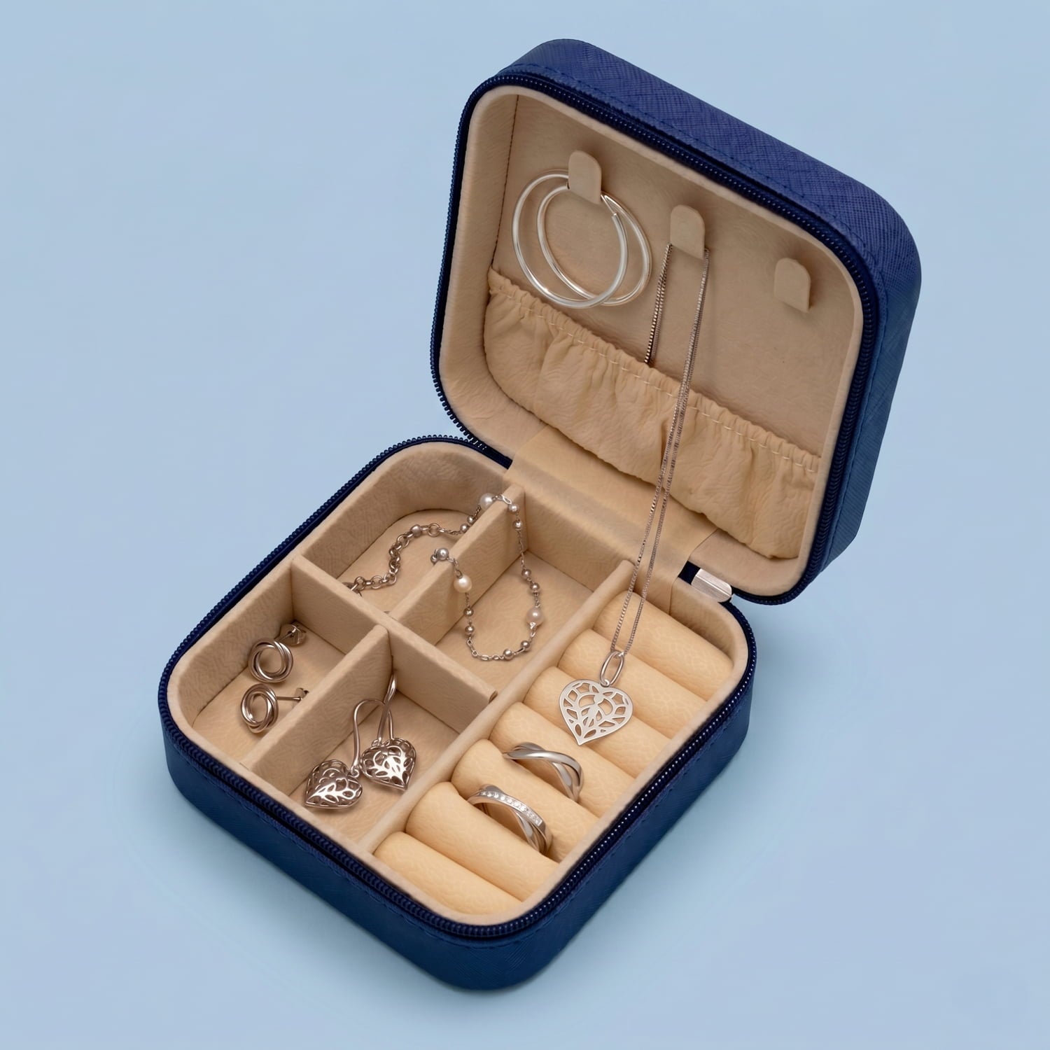 Open navy jewellery box with various silver jewellery items on a light blue background