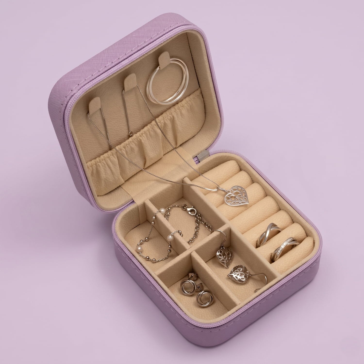 Open lilac jewellery box with various pieces of jewellery on a light purple background