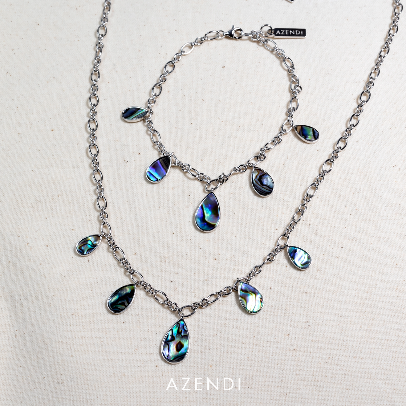 Set of sterling silver jewellery featuring teardrop-shaped abalone shell charms suspended from a polished chain, showcasing iridescent blue, green, and purple tones.
