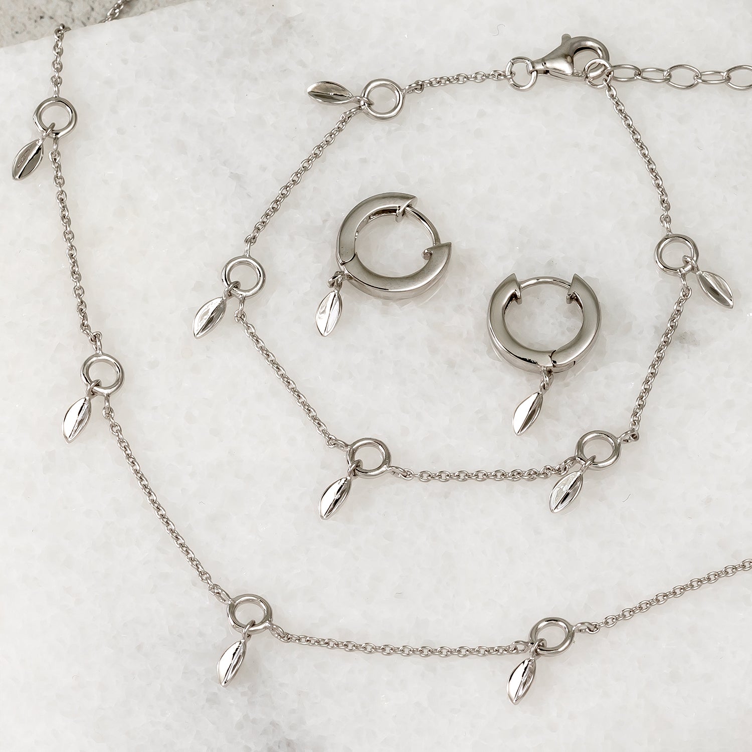 Sterling silver hinged hoop earrings and matching chain necklace featuring delicate leaf-shaped charms, showcasing elegant and refined silver jewellery by Azendi.