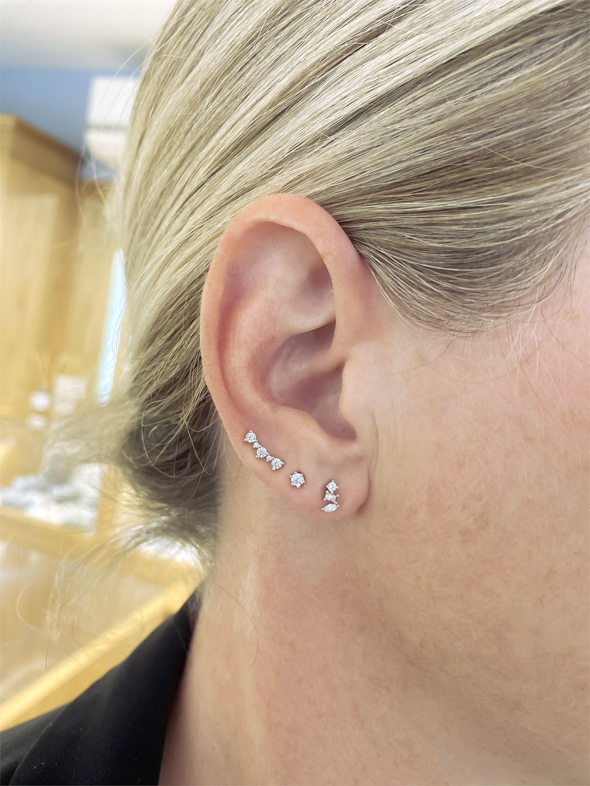Close-up of an ear adorned with delicate silver cubic zirconia studs in curved and geometric shapes, showcasing refined sterling silver jewellery with a modern sculptural aesthetic.