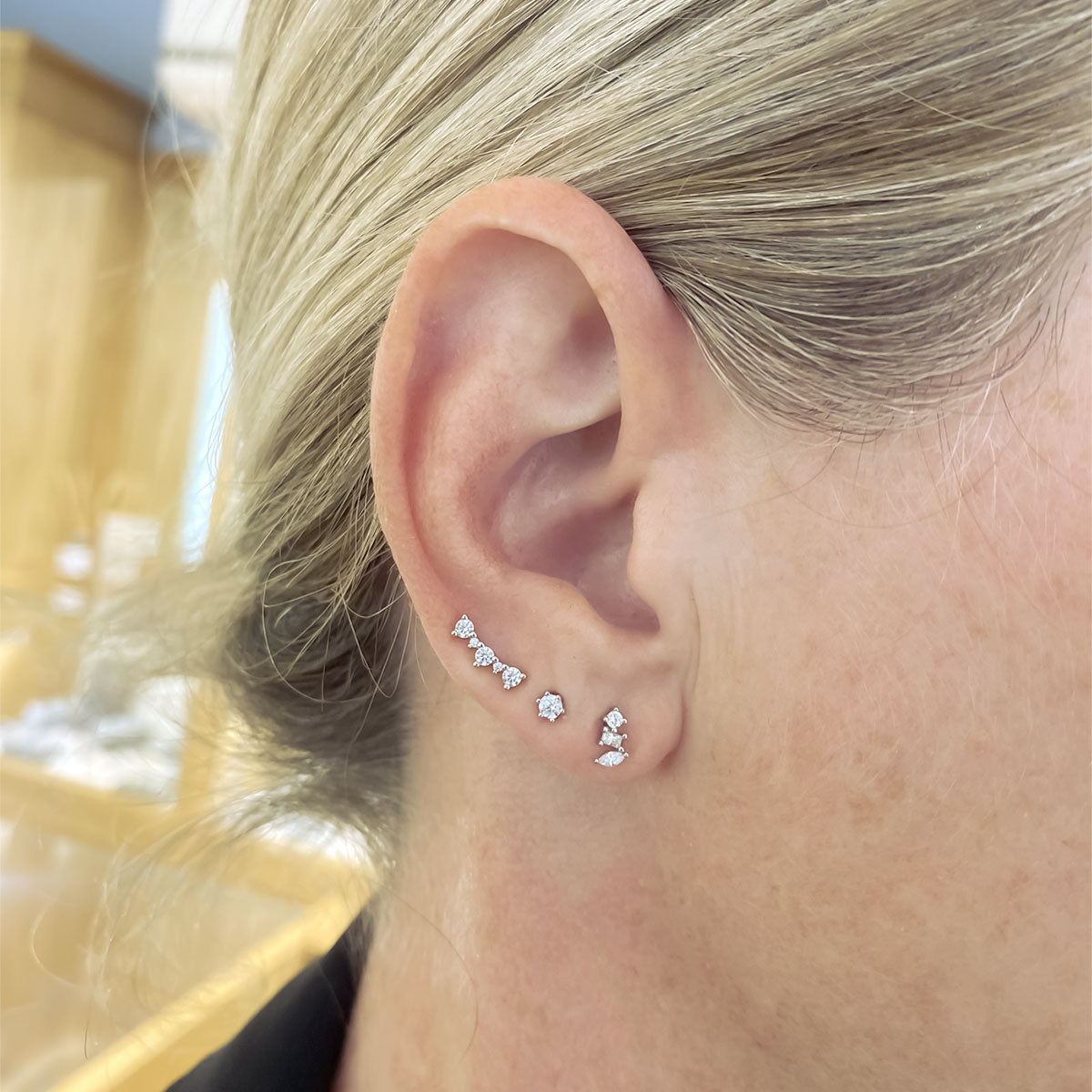 Close-up of an ear adorned with delicate silver cubic zirconia studs in curved and geometric shapes, showcasing refined sterling silver jewellery with a modern sculptural aesthetic.