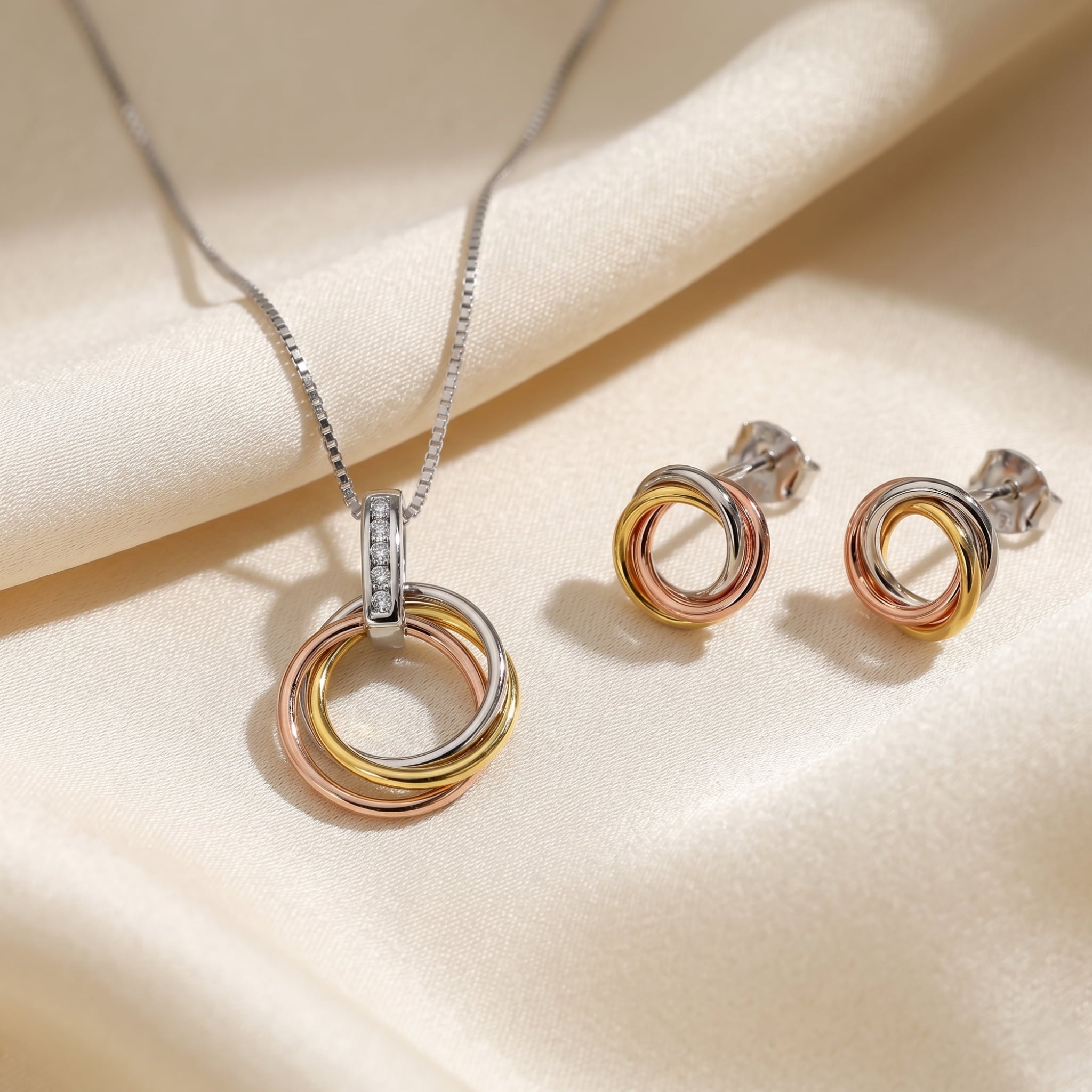 Mixed vermeil pendant and stud earrings featuring intertwined circular loops in rose, yellow, and white gold tones with a delicate diamond-set bale on the pendant.
