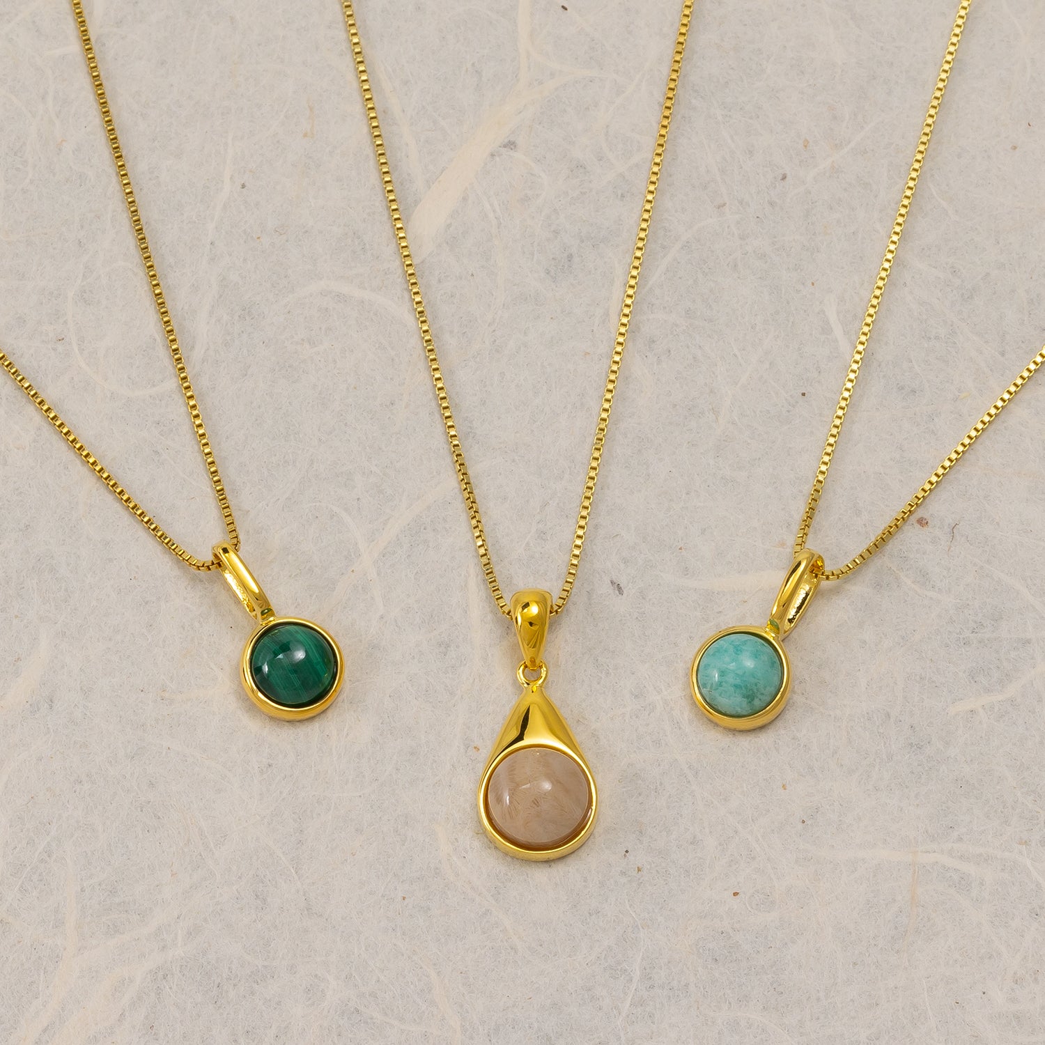 Three gold vermeil pendant necklaces featuring round and teardrop-shaped semi-precious stones in green, peach, and turquoise tones, displayed on a neutral background.
