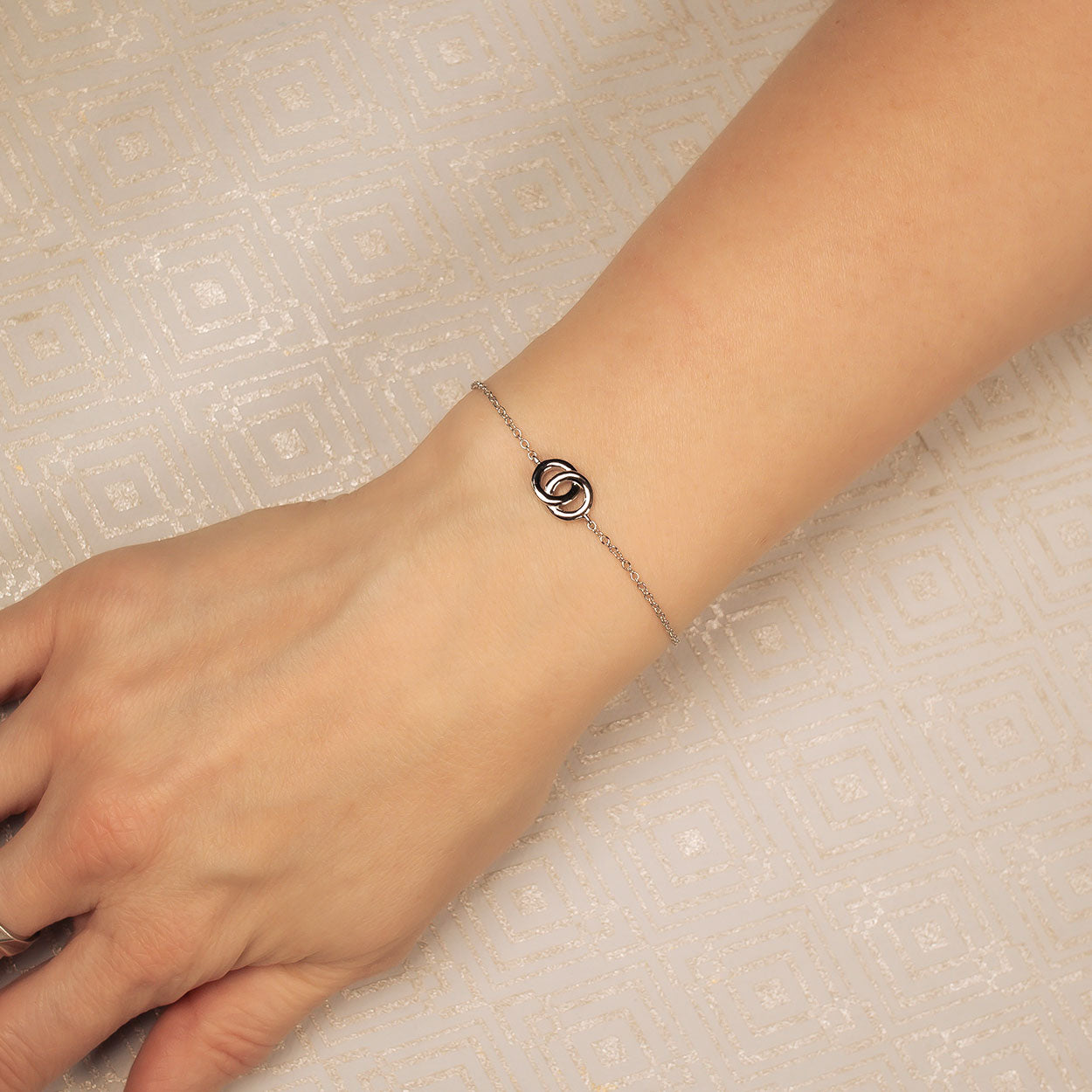 Delicate sterling silver friendship bracelet featuring a sculptural interlocking circles motif on a fine chain, worn elegantly on the wrist.