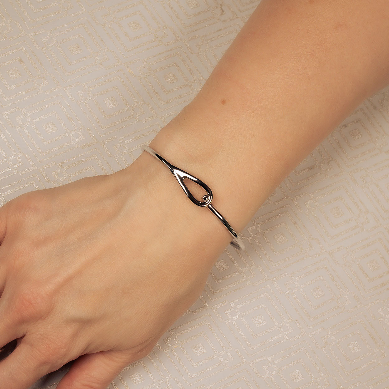 Sterling silver bangle featuring a minimalist open hook loop design, resting elegantly on the wrist to highlight refined contemporary British silver jewellery.