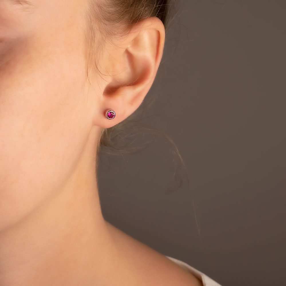 Delicate sterling silver stud earrings featuring deep red ruby gemstones, designed to offer a subtle yet elegant touch of July birthstone luxury.