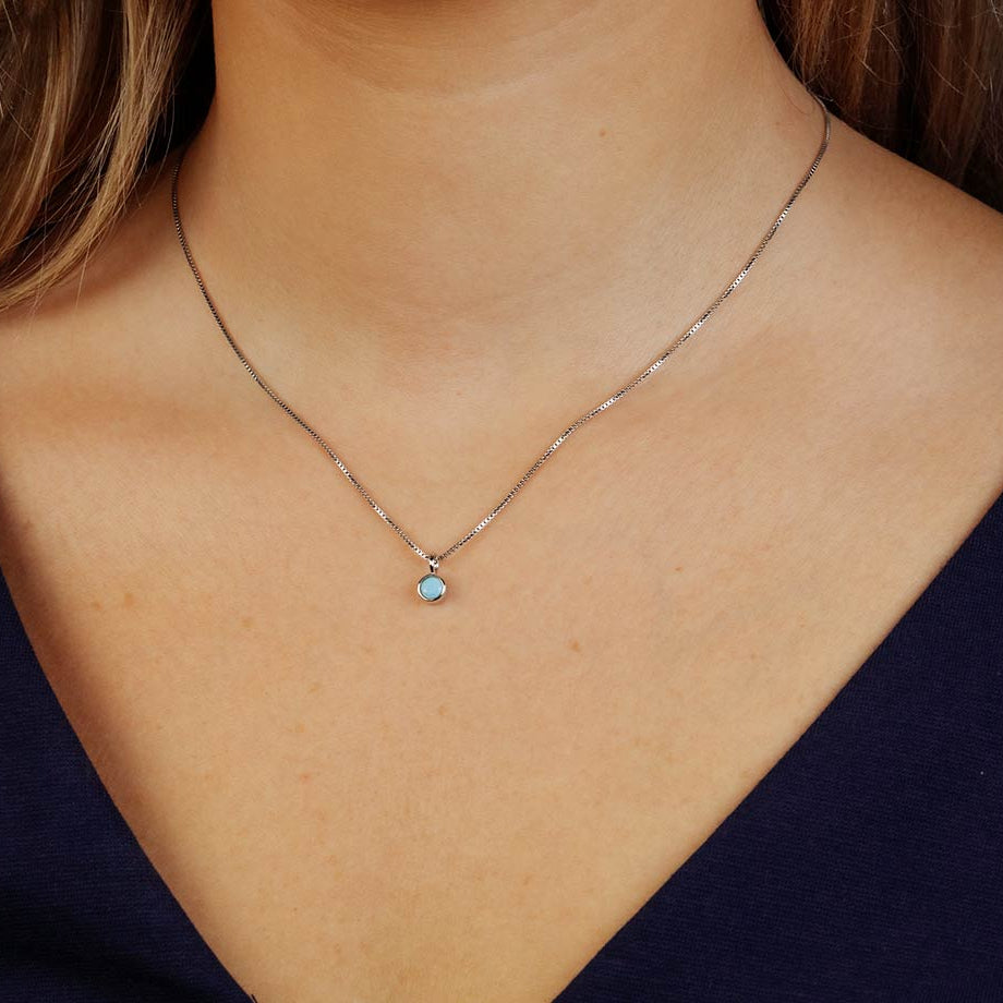 Delicate sterling silver necklace featuring a small turquoise pendant with a minimalist design, styled against a deep navy top for a refined look.