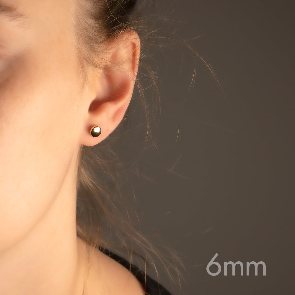 Pair of yellow gold vermeil button stud earrings with a smooth double curved surface, showcasing a minimalist and sculptural design on the earlobe.