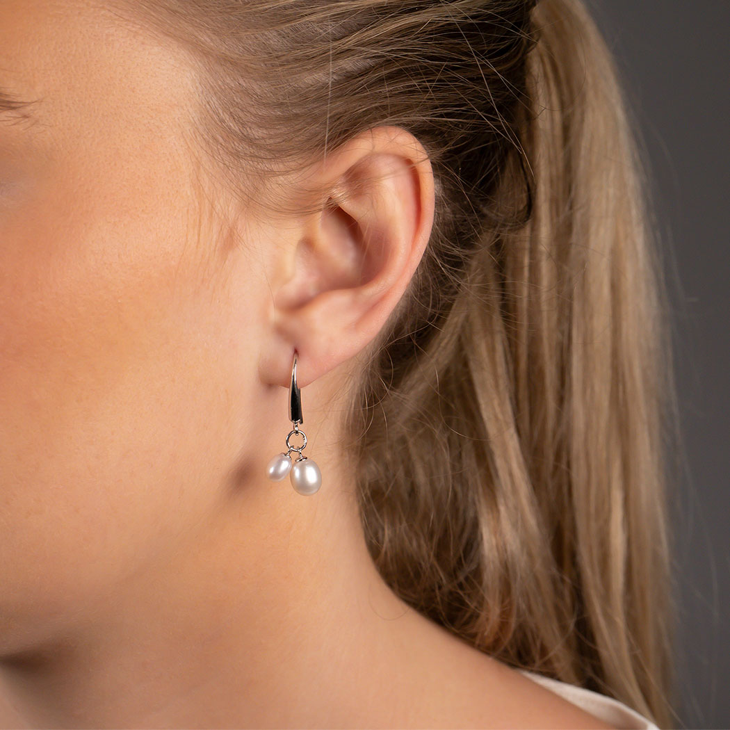 Elegant sterling silver drop earrings featuring twin teardrop freshwater pearls suspended from sleek hooks, worn on a model against a neutral grey background.