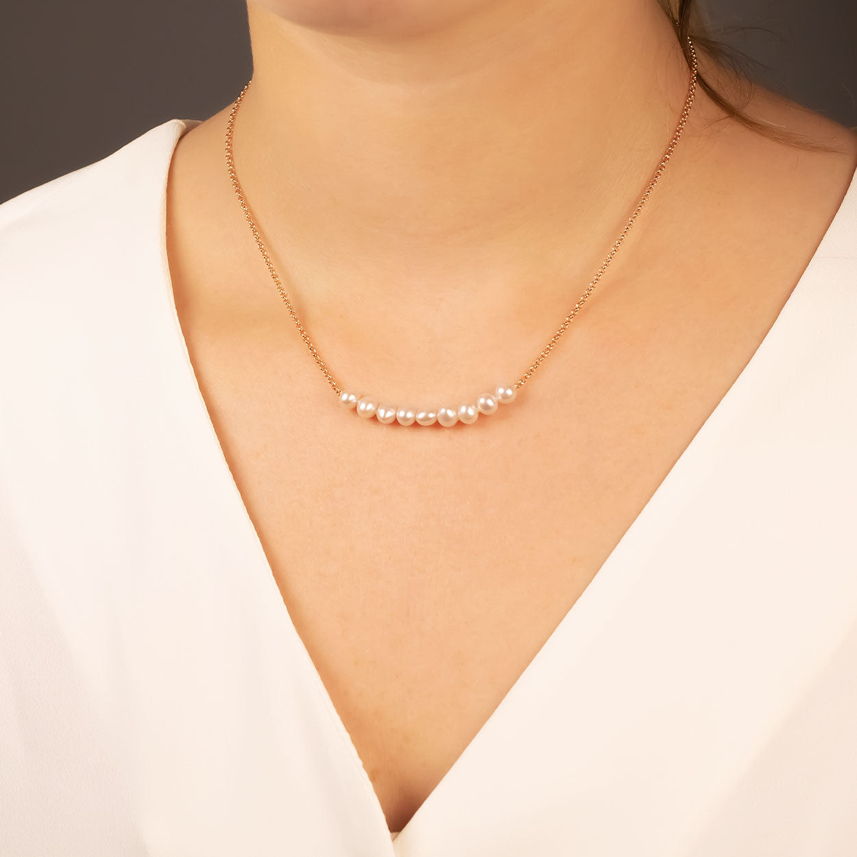 Close-up of a woman wearing a delicate necklace featuring nine lustrous pearls on a fine gold vermeil chain, styled with a soft white blouse for an elegant look.