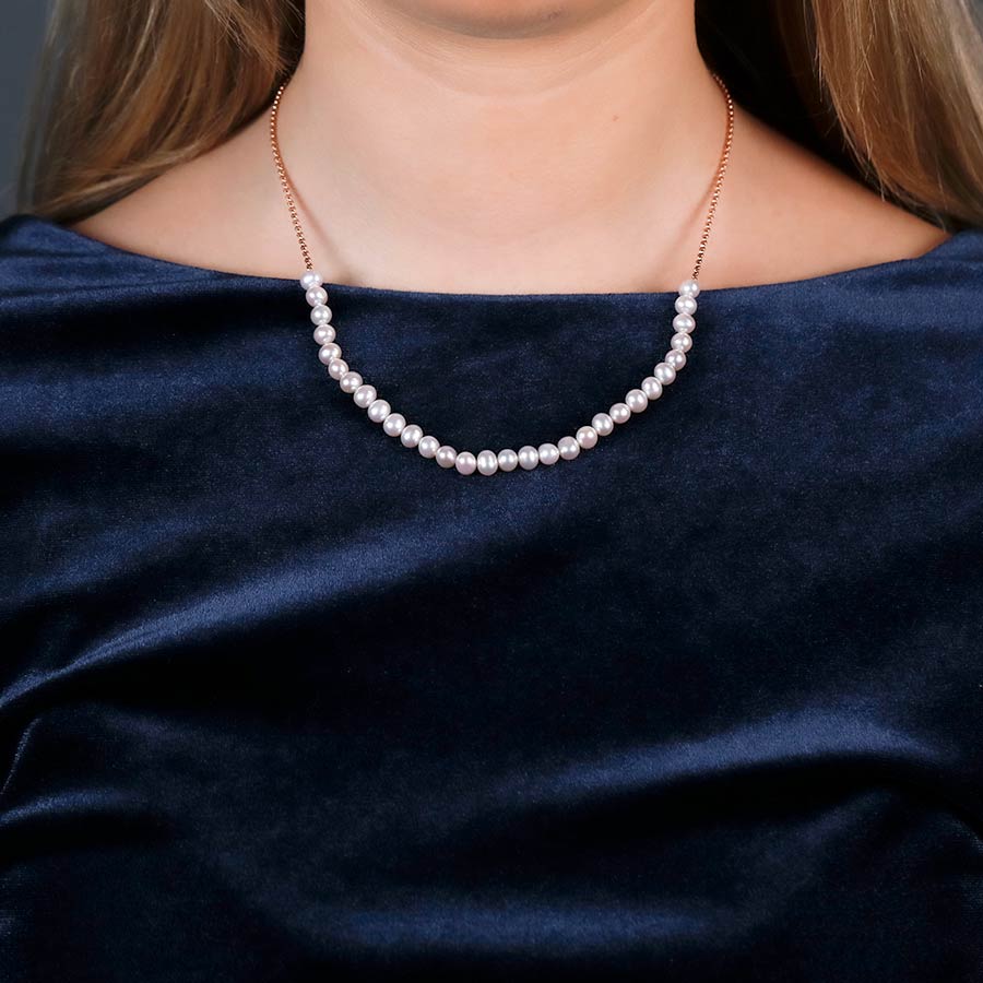 Woman wearing a delicate pearl strand necklace featuring thirty lustrous pearls on a fine chain, styled against a deep navy satin top for an elegant finish.