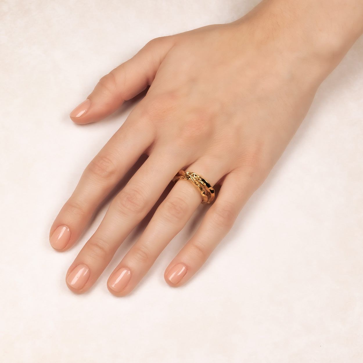 Close-up of a hand wearing a hammered textured sterling silver wedding band with a warm golden finish, showcasing contemporary designer jewellery by Azendi.