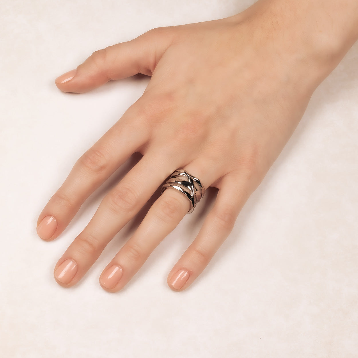 Wide sterling silver ring with a hammered textured crossover design, showcasing a bold sculptural style on a slender hand for a contemporary statement piece.