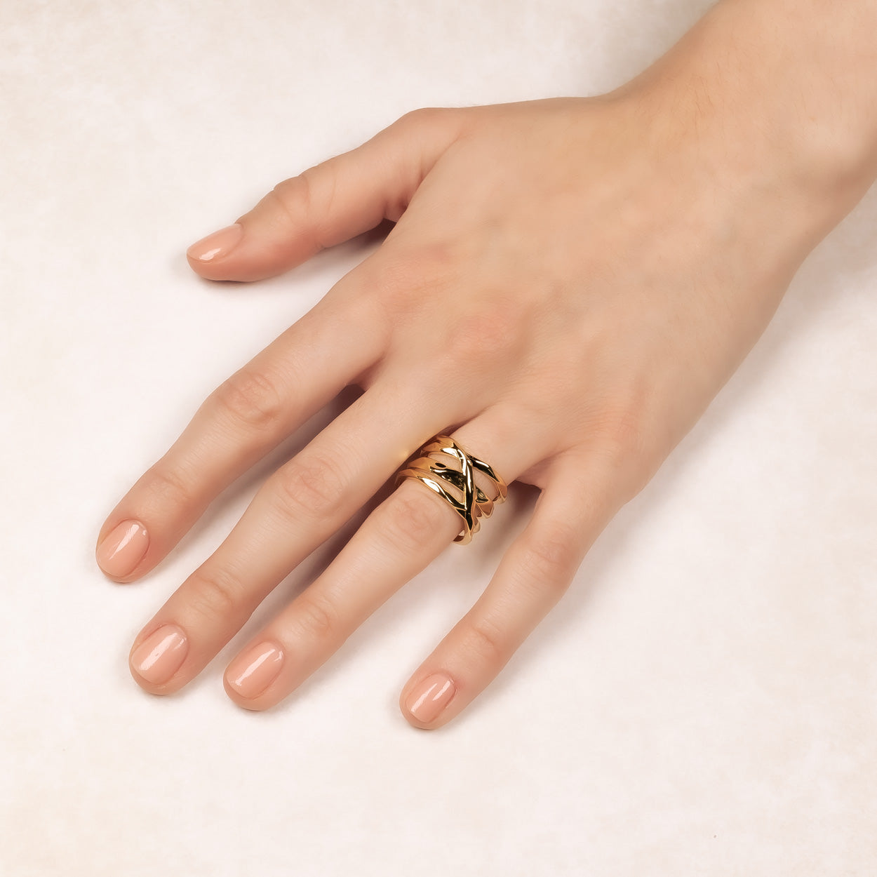 Wide sterling silver ring with a hammered finish featuring an elegant crossover design, worn on a hand with a neutral polish for a modern, sculptural look.