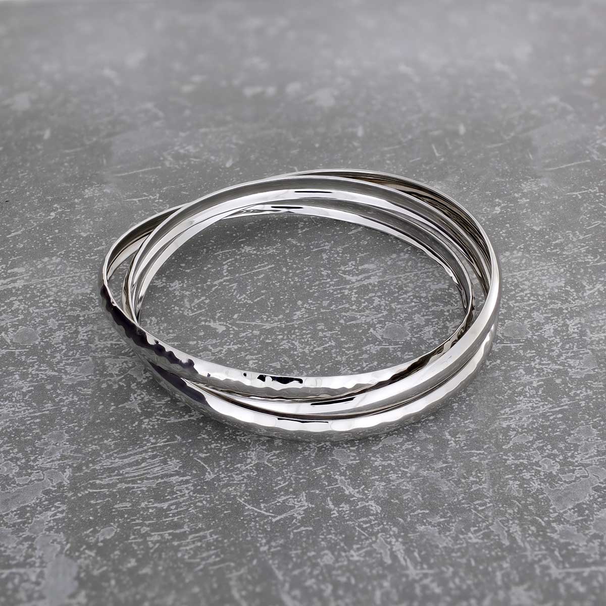Set of three interlocking sterling silver bangles with textured surfaces, showcasing a modern and sculptural design in polished silver jewellery.