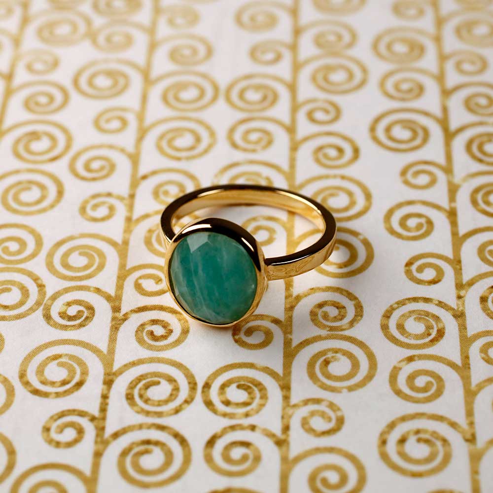 Yellow gold vermeil ring showcasing a smooth oval amazonite stone set on a polished band, placed against a decorative patterned background for a contemporary look.