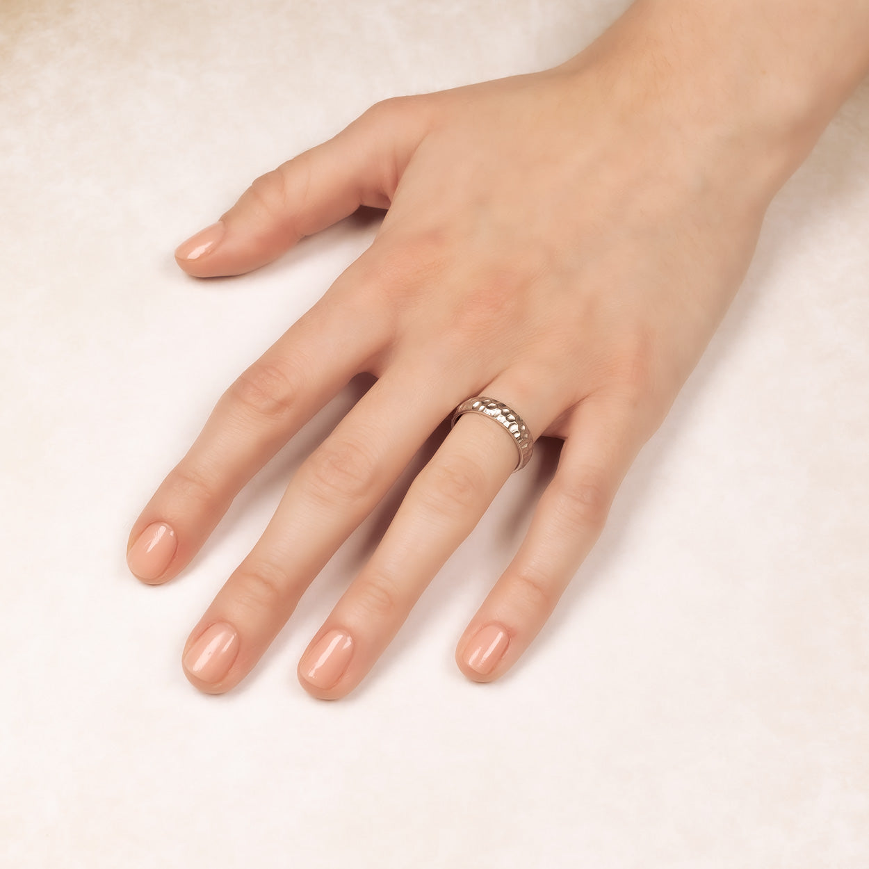 Hand wearing a sterling silver satin hammered ring with a textured surface, highlighting a handcrafted sculptural design by a British designer for contemporary silver jewellery collections.