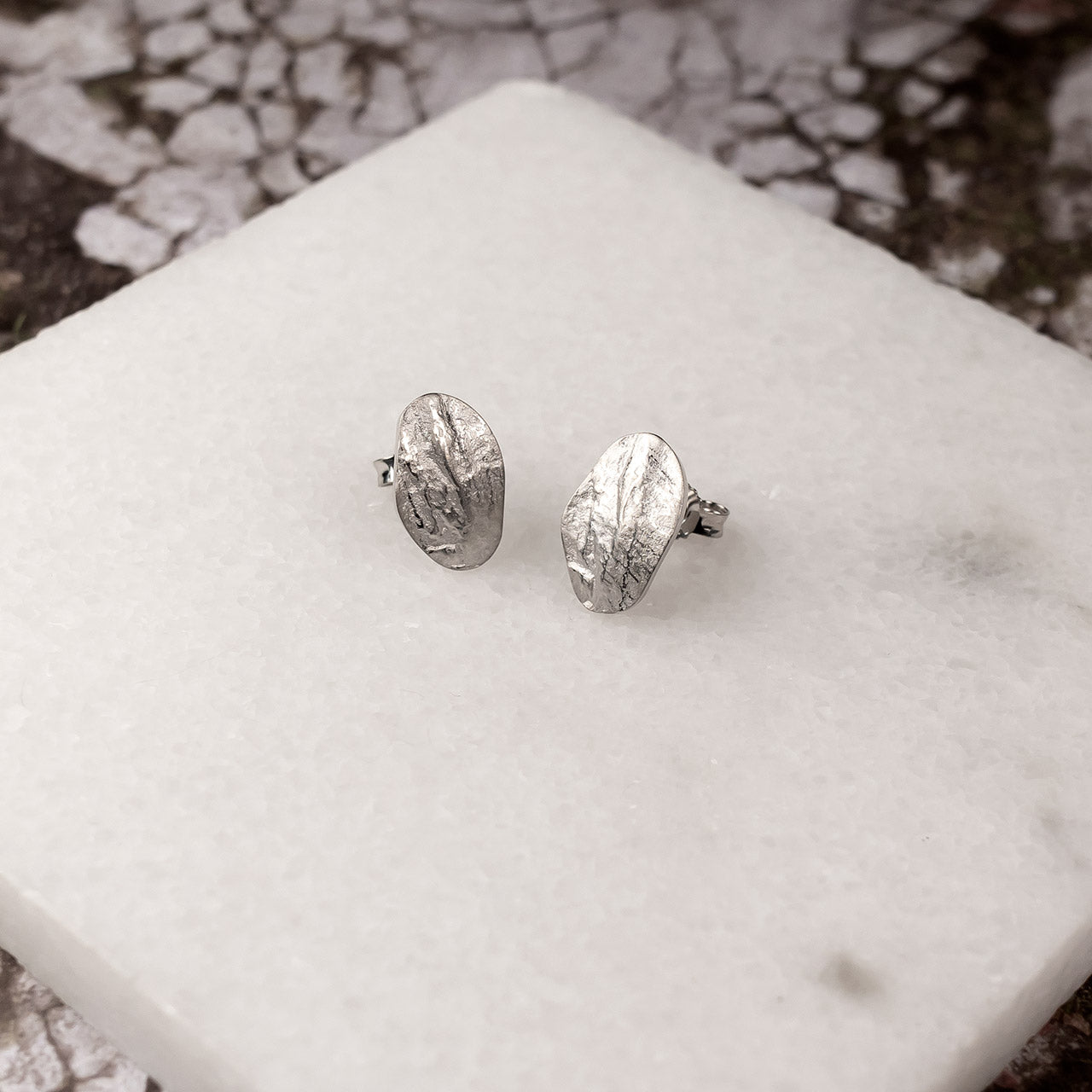 Oval sterling silver stud earrings featuring a textured, sculptural surface inspired by natural forms, showcasing unique contemporary British silver jewellery design.